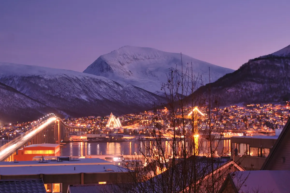Το Tromsø στην πολική νύχτα το λυκόφως, με φωτισμένους δρόμους, τη γέφυρα και χιονοσκεπασμένα βουνά κάτω από έναν μοβ ουρανό